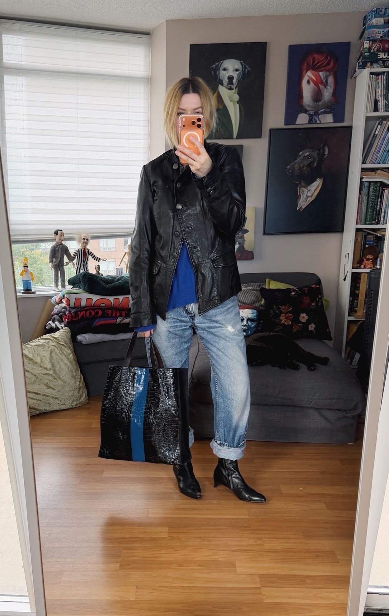Sara of livelovesara is standing in front of a mirror taking a photo of her outfit. She is wearing a cobalt blue vintage Ralph Lauren sweater under a vintage asymmetric fron leather jacket, vintage levis cuffed over black heeled boots, and is carrying a striped Dries Van Noten bag.