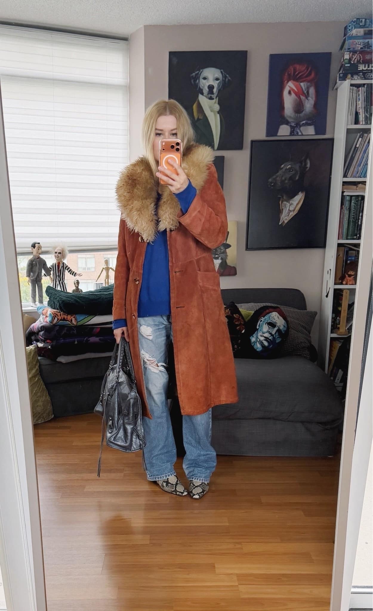 Sara of livelovesara is standing in front of a mirror taking a photo of her outfit. She is wearing a cobalt blue vintage Ralph Lauren sweater with vintage levis, a vintage suede trench with a fur collar, snake print boots, and a balenciaga grey city bag,
