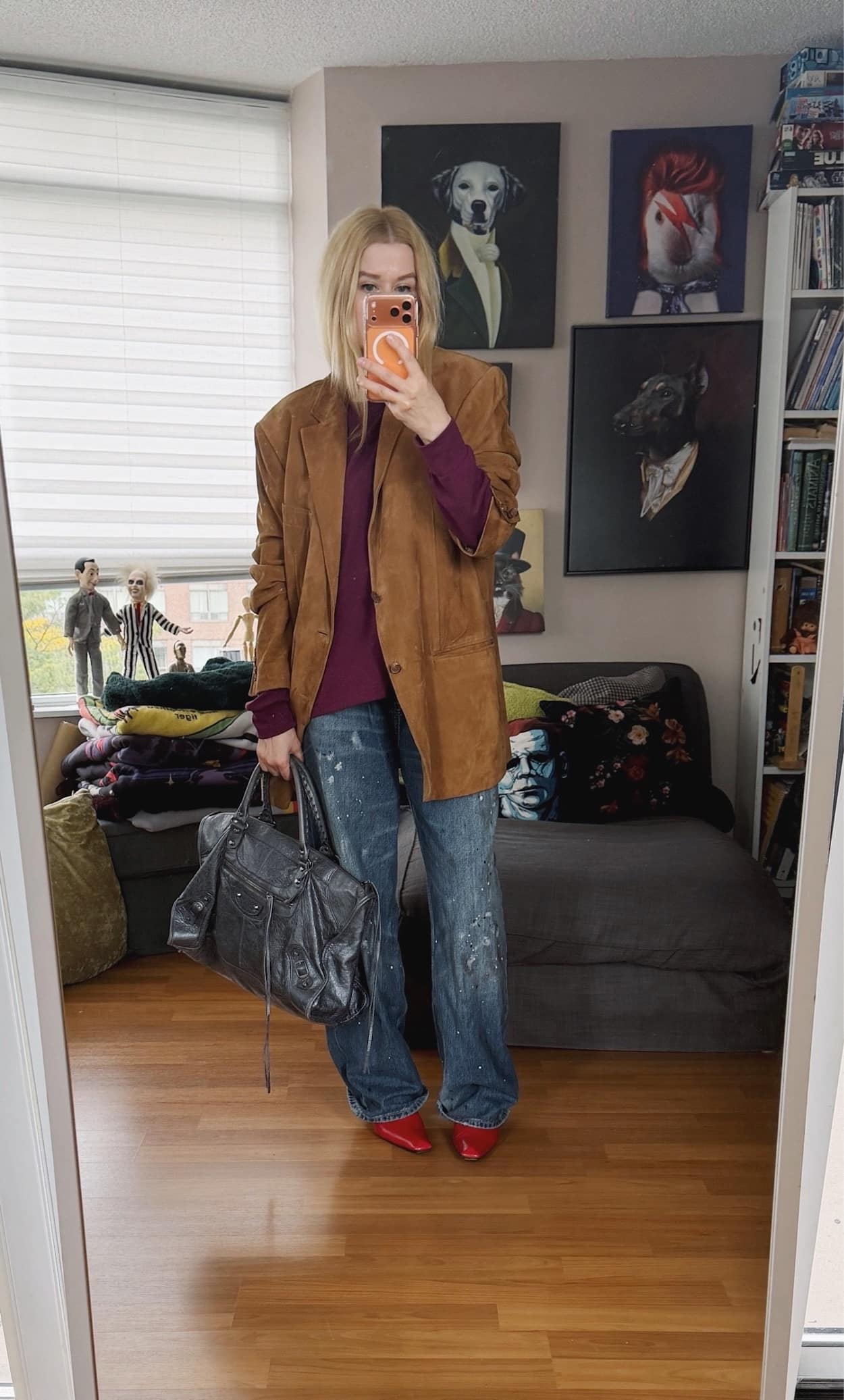 Sara of livelovesara is standing in front of a mirror taking a photo of her outfit. She is wearing a purple sweater under a cognac suede vintage Ralph Lauren blazer, paint splatter jeans, red vintage boots, and is carrying a large grey Balenciaga city work bag.