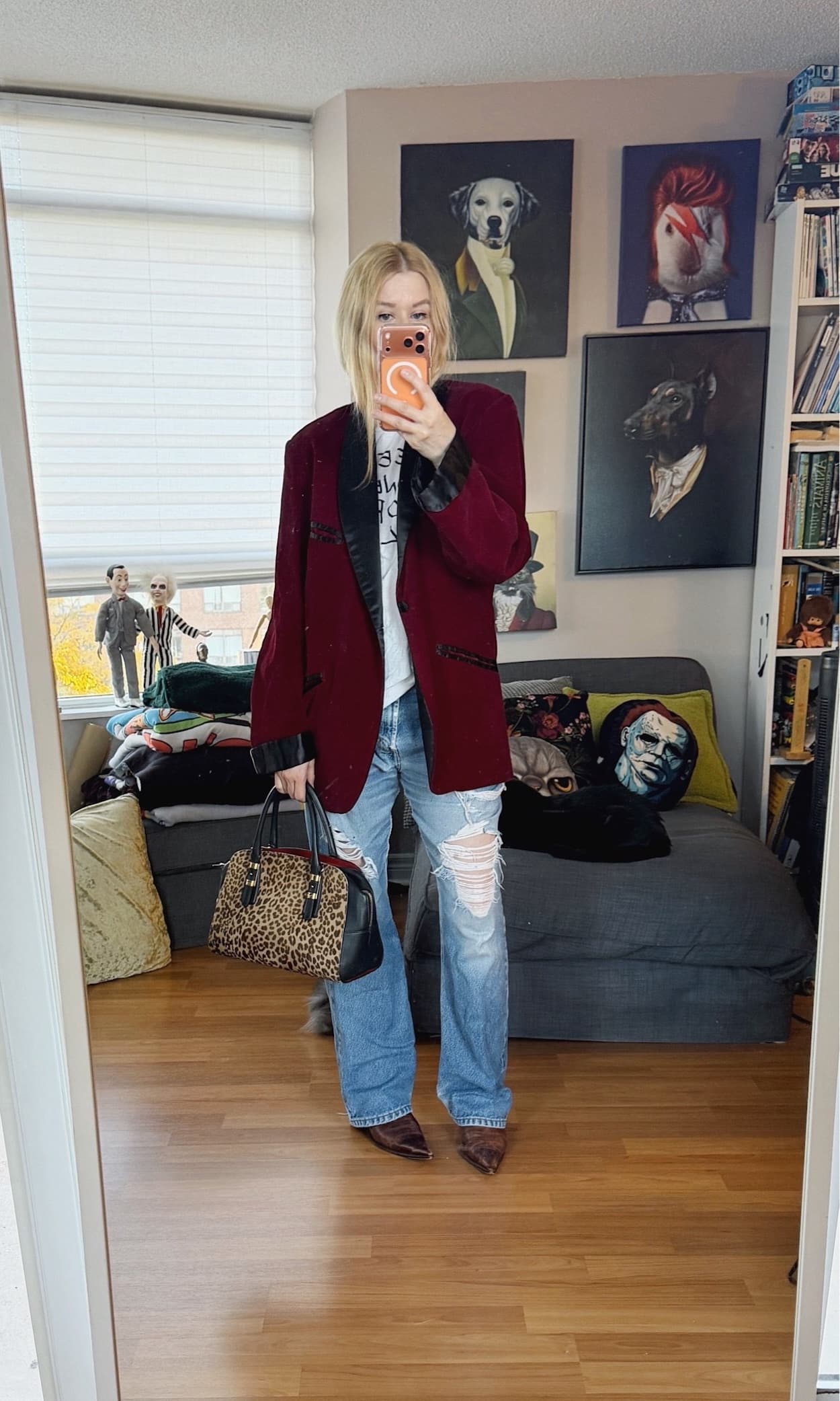 Sara of livelovesara is standing in front of a mirror taking a photo of her outfit. She is wearing a white tee under burgundy velvet smoking jacket, vintage Levis, brown vintage boots, and is carrying an animal print bag.