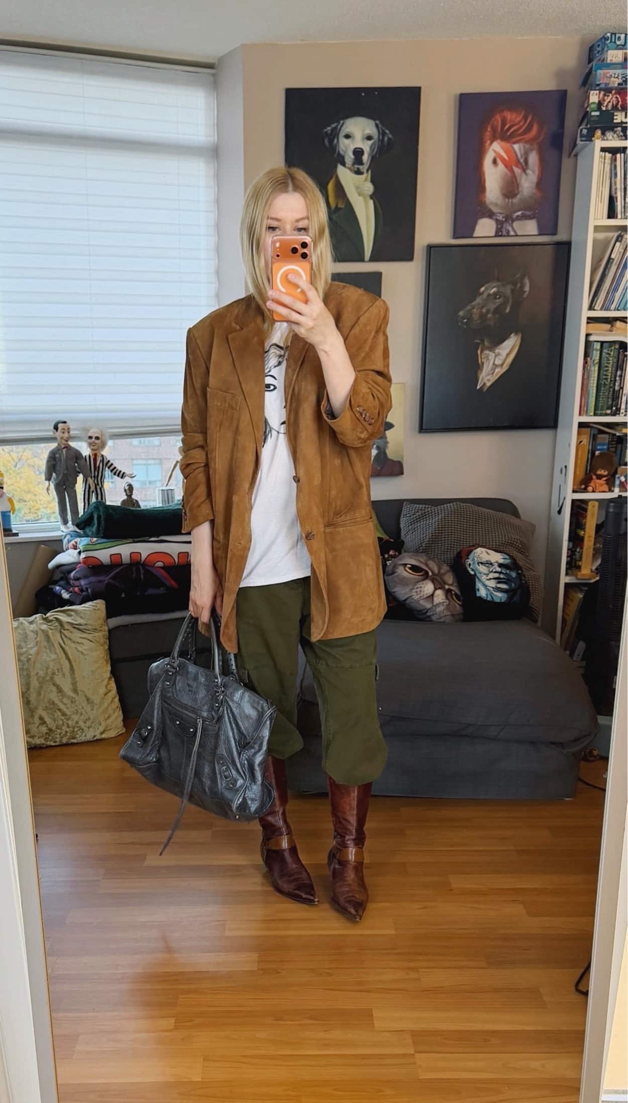Sara of livelovesara is standing in front of a mirror taking a photo of her outfit. She is wearing a Kim Gordon tee under an oversized tab suede blazer, cargo pants tucked into brown vintage boots, and is carrying a grey balenciaga work bag.