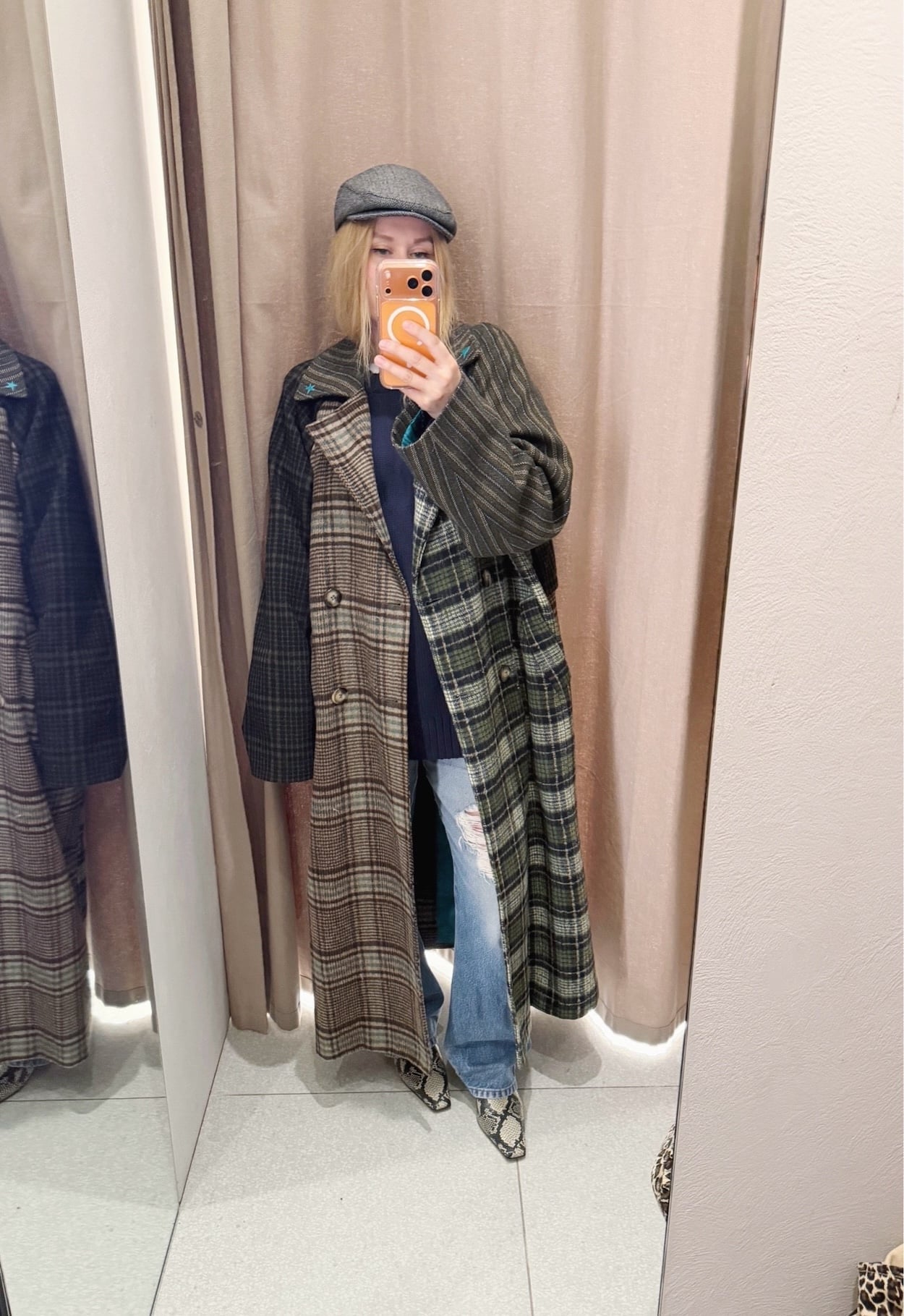 Sara of livelovesara is standing in front of a mirror taking a photo of her outfit. She is wearing a navy blue sweater and vintage Levis under a multi colour plaid long coat, a grey herringbone cap, and snake print boots.