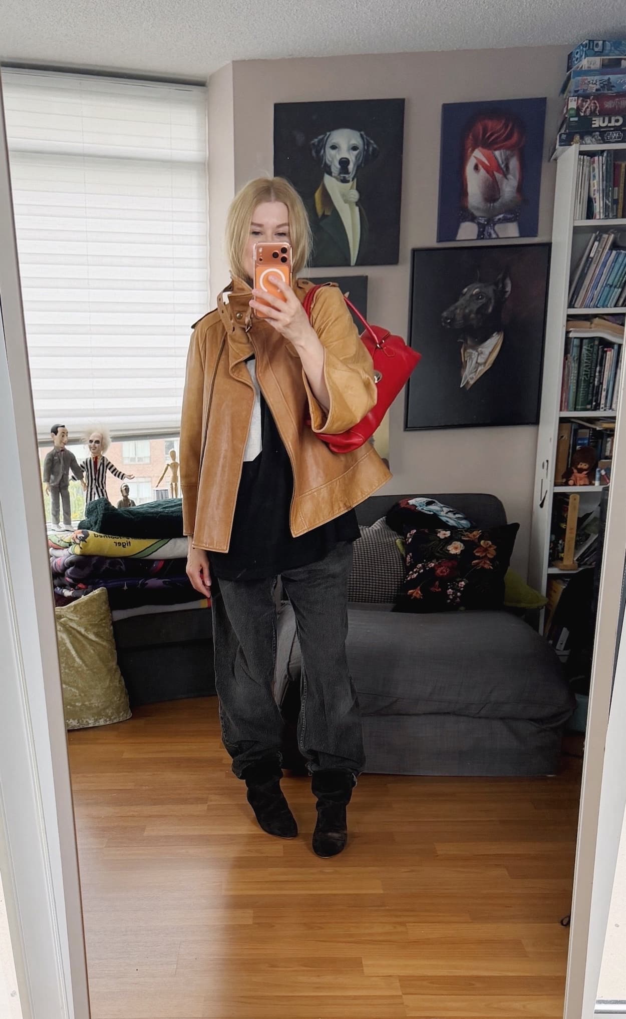 Sara of livelovesara is standing in front of a mirror taking a photo of her outfit. She is wearing an FU t-shirt with black vintage Levi's, a tan funnel neck vintage leather jacket, black slouch boots, and a red Prada bag.